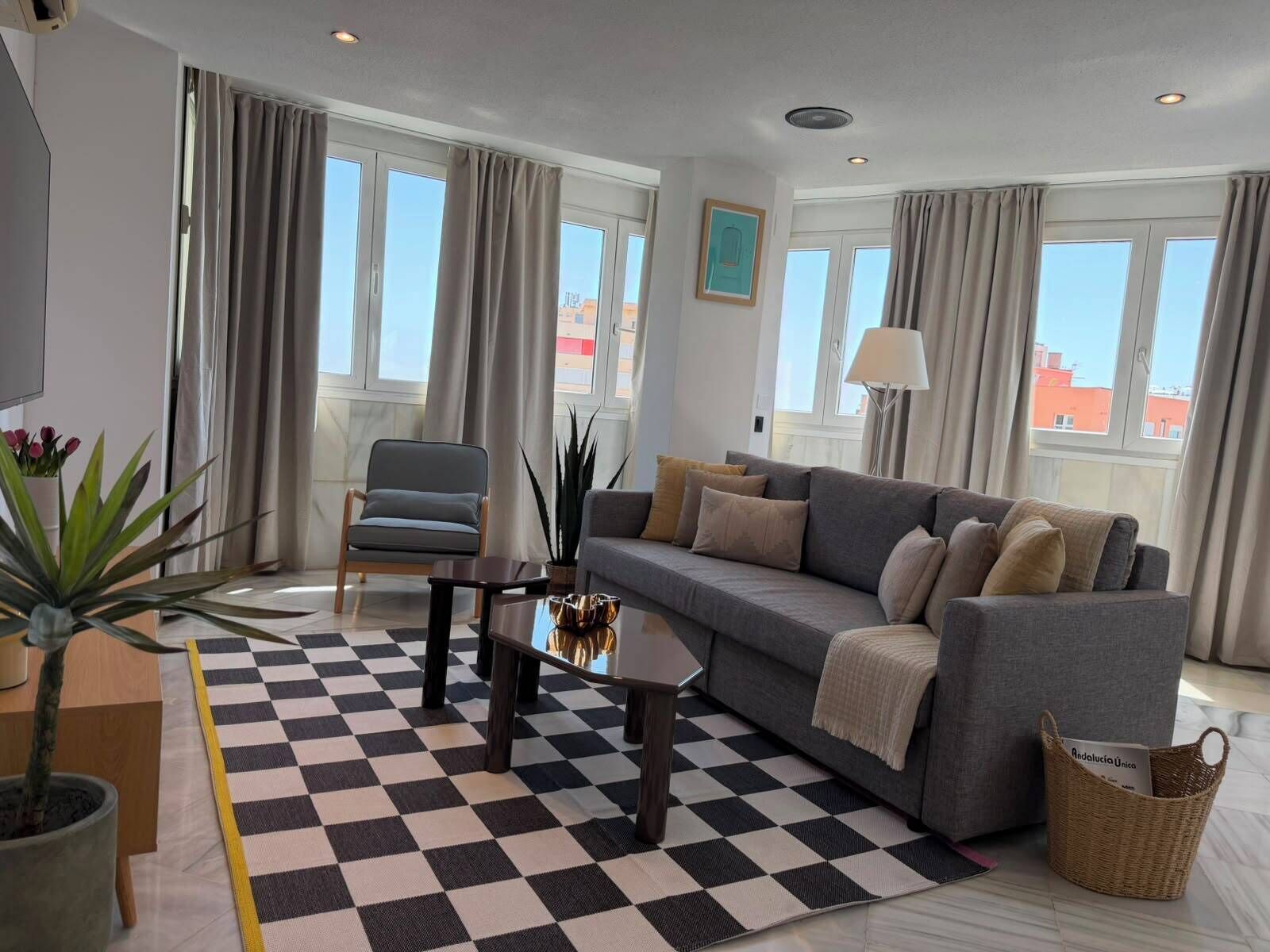 Een moderne woonkamer met een zwart-wit betegelde vloer, een grijze bank, een houten stoel, een klein tafeltje en een potplant.