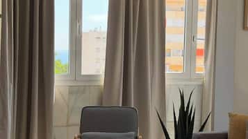 Un salon comprenant un canapé, un fauteuil, une table basse et une grande fenêtre avec des rideaux.