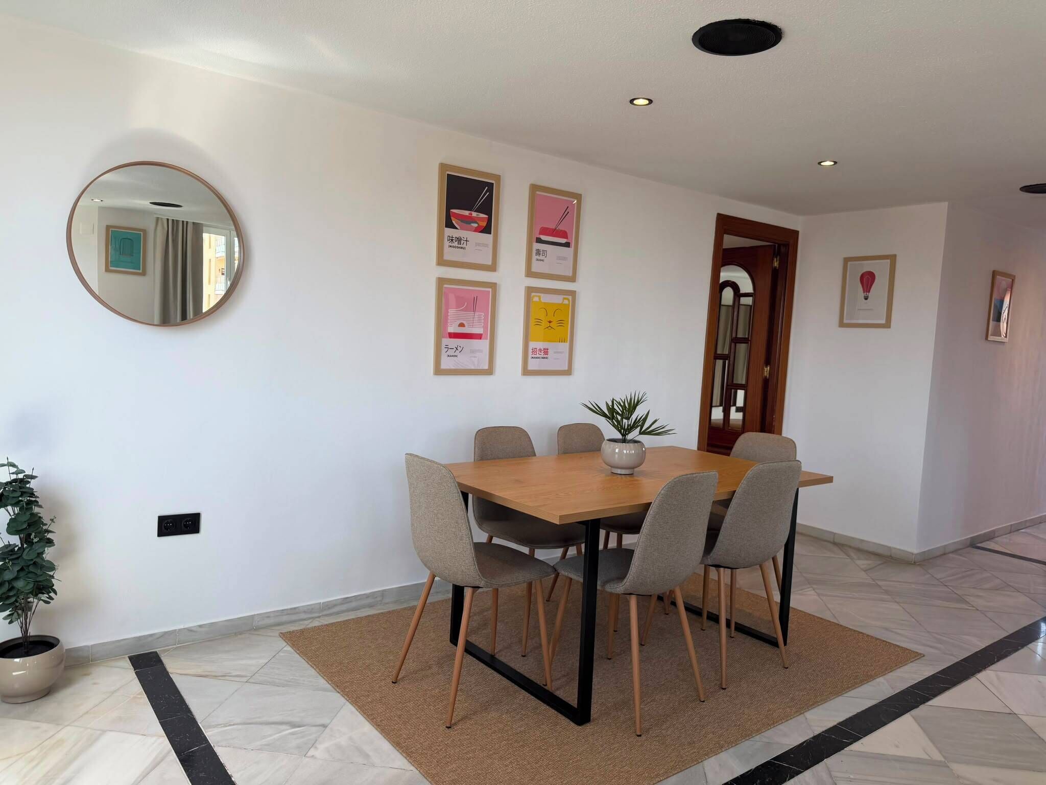 Un coin repas avec une table en bois et six chaises, une plante en pot et un miroir au mur.