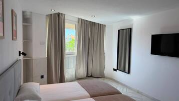 A hotel room with a bed, a TV mounted on the wall, and a window with curtains.