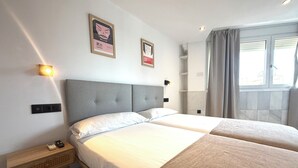 Et hotelværelse med en dobbeltseng, sengeborde, en lampe på væggen og et vindue med gardiner.