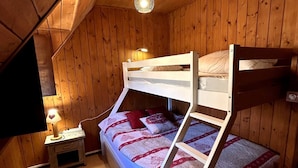 A bunk bed room with wooden walls, a ceiling light, and a bedside table with a lamp.