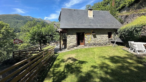A stone house with a sloped roof, a wooden deck, and a grassy yard.