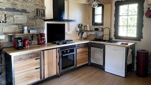 A compact kitchen with a stone wall, wooden cabinets, a built-in oven, a dishwasher, and a window with a view.