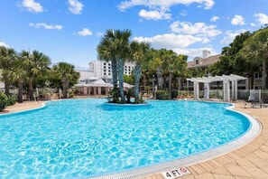 Une piscine dont la profondeur maximale est indiquée à 4 pieds, entourée de palmiers et bordée d’un bâtiment à la façade blanche.