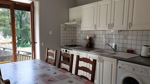 Una cucina con mobili bianchi, un tavolo da pranzo con tovaglia, una lavatrice e vista sull'esterno.