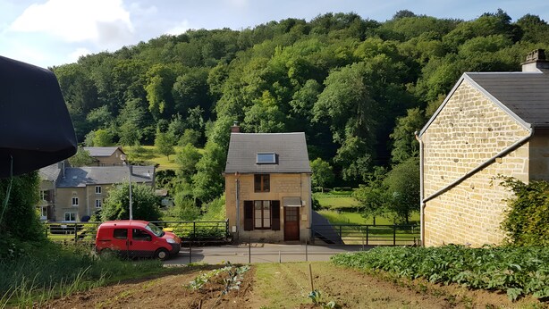 Una casa di campagna con facciata in pietra, un piccolo giardino e un'auto rossa parcheggiata davanti.