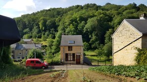 Una casa rural con fachada de piedra, un pequeño jardín y un coche rojo estacionado adelante.