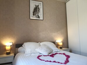 Una habitación de hotel con una cama, dos lámparas de noche, un cuadro en la pared y un adorno con forma de corazón sobre la cama.