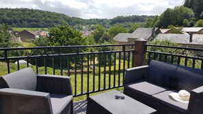 Ein Balkon mit Gartenmöbeln, Blick auf eine grüne Landschaft und einen klaren Himmel.