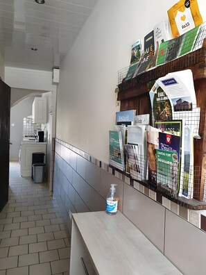 Un pasillo con una mesa de recepción, un bote de basura y una pared con varios carteles informativos.