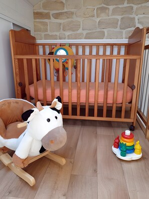 Ein hölzernes Kinderbett mit weichem Bettzeug, ein Schaukelpferd und ein Spielzeug-Stapelring.