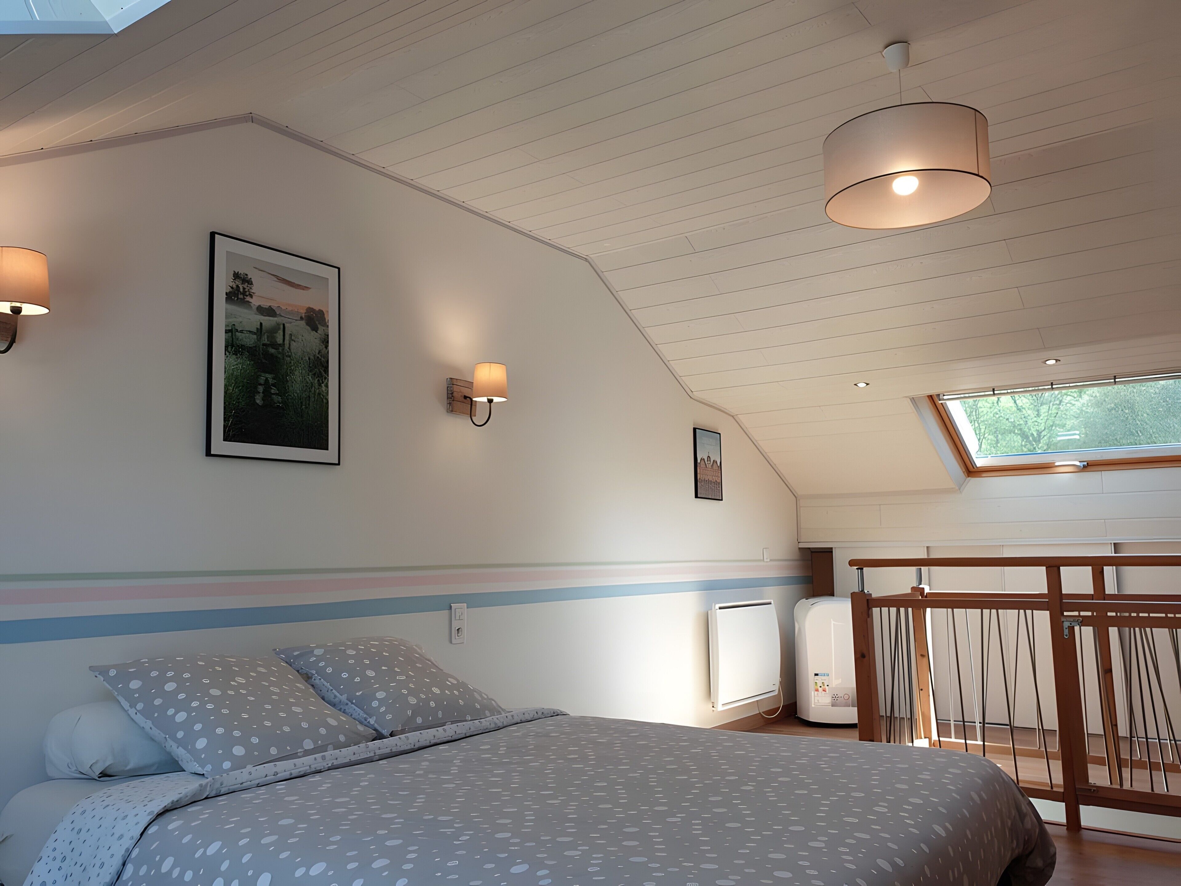 A bedroom with a bed, two wall-mounted lamps, a framed picture, a radiator, and a skylight.