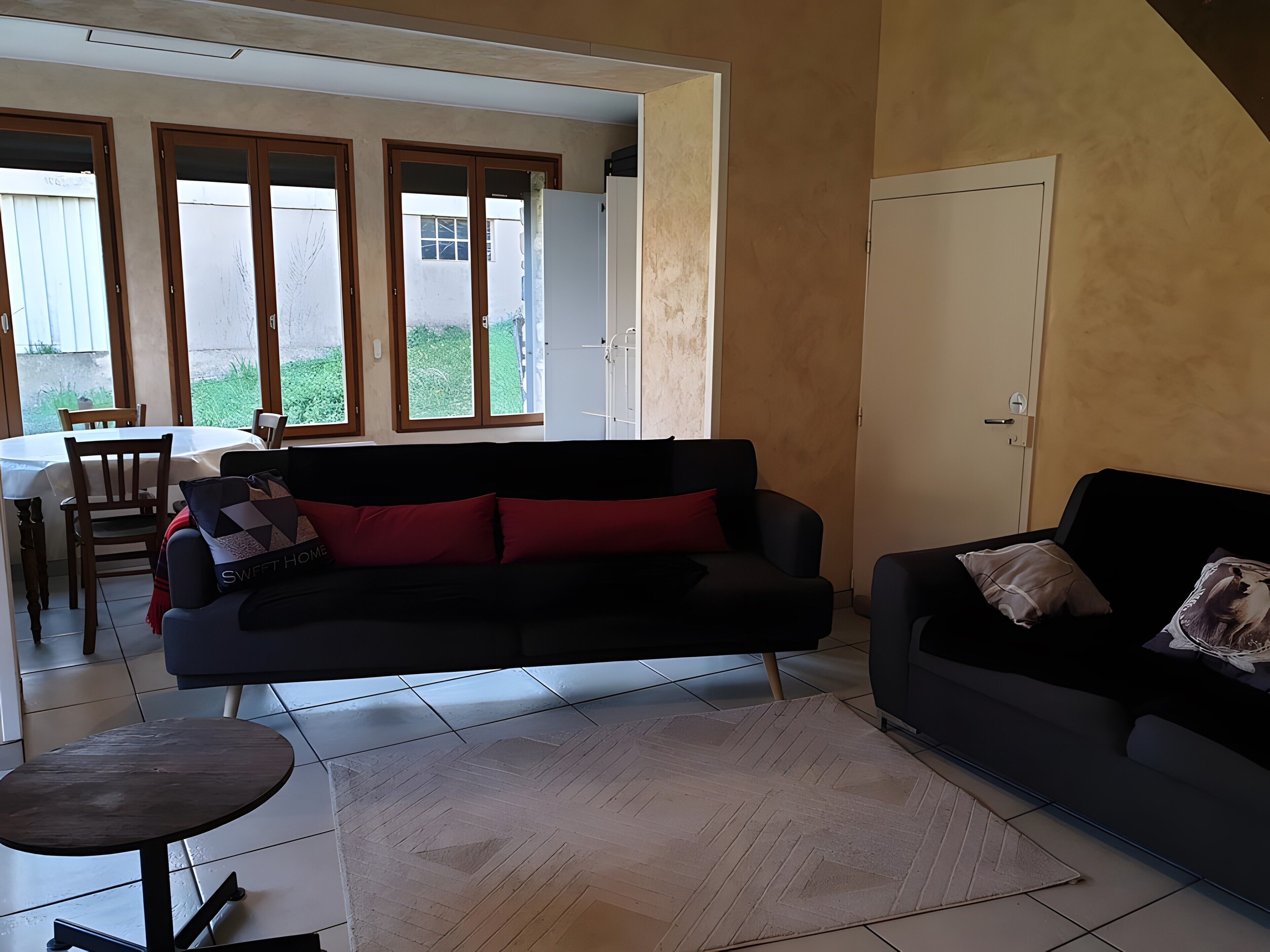 A living room with a black sofa, a small round table, and a dining area with a table and chairs.