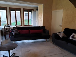 Ein Wohnzimmer mit einer schwarzen Couch, einem kleinen runden Tisch und einem Essbereich mit Tisch und Stühlen.