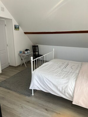 A bedroom with a white bed, a small table with a chair, and a door.