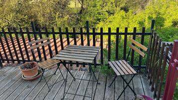 A wooden deck with a table and benches, surrounded by a black fence and lush greenery.