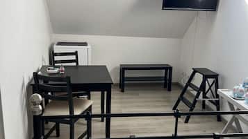 Ein kleiner, privater Raum mit einem Bett, einem Tisch, einem Stuhl, einer Bank, einem Fernseher und einem Dachfenster.