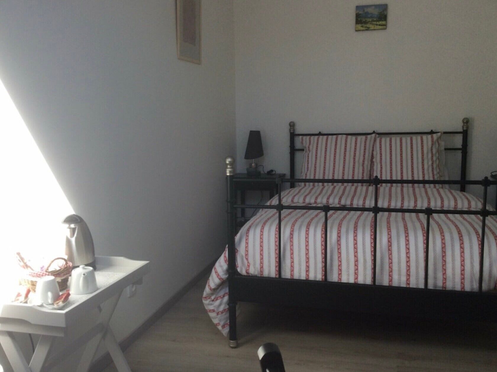 Une chambre à coucher avec un lit, une table de chevet, une lampe et un petit tableau accroché au mur.