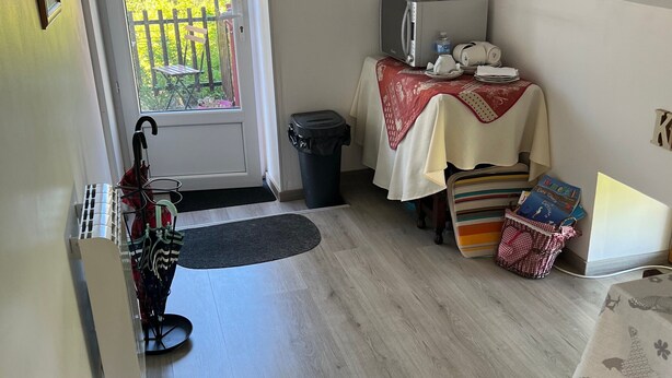 Pieni ja käytännöllinen keittiö, jossa on mikroaaltouuni, pieni pöytä punaisella pöytäliinalla sekä ovi, josta avautuu näkymä puutarhaan.