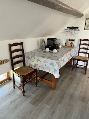 A dining area with a table set for two, a coffee maker, and a bottle of water.