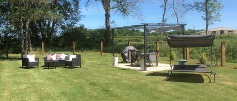 Een terras buiten met een pergola, een barbecue en zitplaatsen.