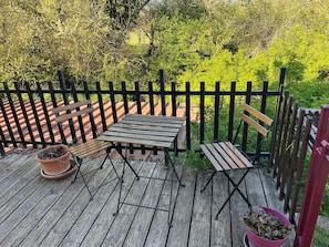 A wooden deck with a table and benches, surrounded by a black fence and lush greenery.