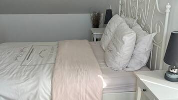 Quarto com cama, mesa de cabeceira, abajur e um criado-mudo com um vaso.