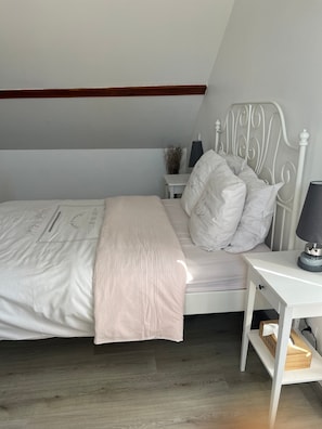 A bedroom with a bed, bedside table, lamp, and a small nightstand with a vase.