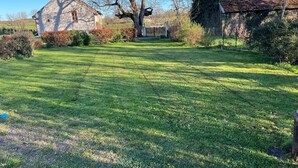 A well-maintained grassy area with a stone building and a wooden fence in the background.