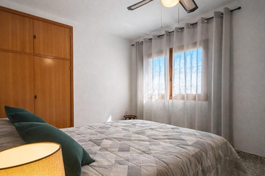 Een slaapkamer met een bed, een houten kledingkast, een nachtkastje en een raam met gordijnen.