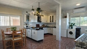 A kitchen with white cabinets, a dining table with chairs, a washing machine, and a window with bars.