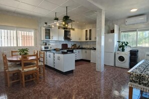 A kitchen with white cabinets, a dining table with chairs, a washing machine, and a window with bars. - Mediterranean Family Home with Private Pool & Panoramic Views (Alguazas)