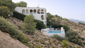 A white building with arched windows and a swimming pool on a hillside.
