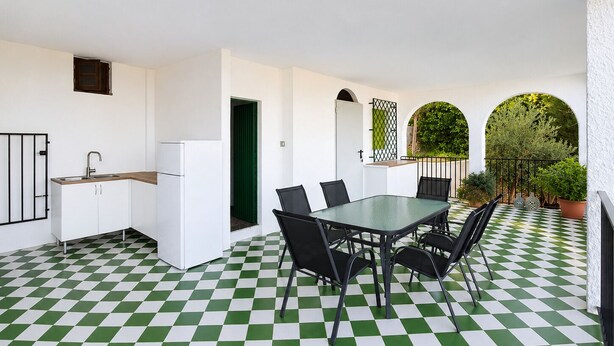 A kitchen with a sink, refrigerator, and white cabinets. There is a dining table with chairs and a checkered floor.