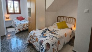 A bedroom with two beds, a wardrobe, a window, and a sloped ceiling.