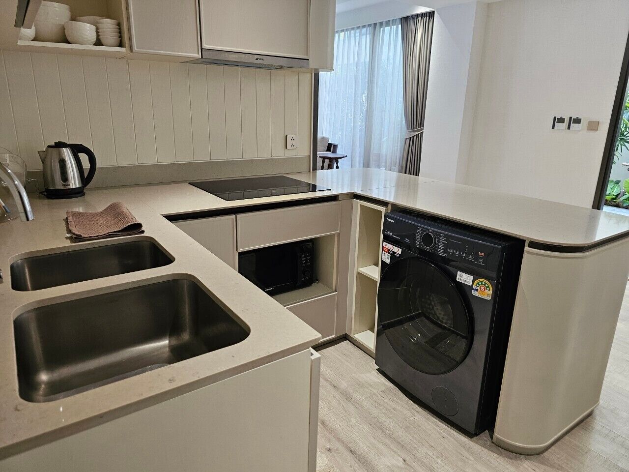 A compact kitchen with a built-in washing machine, a microwave, and a kettle.