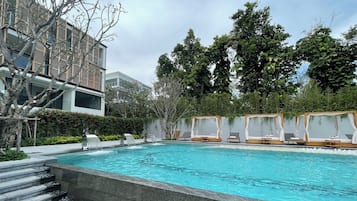 A swimming pool with a stone border, surrounded by lounge chairs and a building with a modern design.
