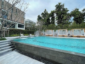 A swimming pool with a stone border, surrounded by lounge chairs and a building with a modern design. - InterCon 3 Bedrooms (Tambon Hua Hin)