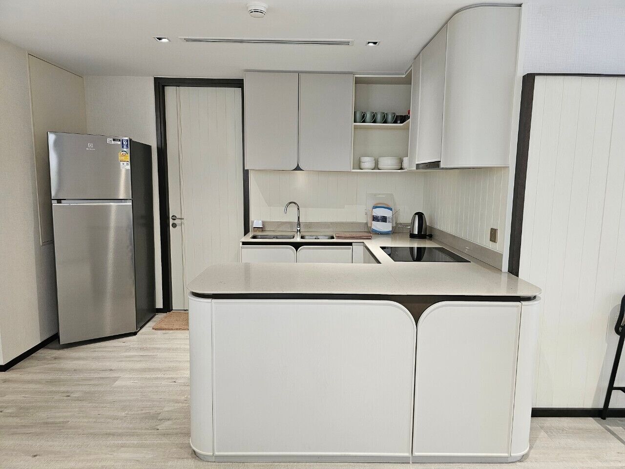 Una cocina moderna con una isla integrada, refrigerador de acero inoxidable y gabinetes blancos.