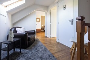 A modern living room with a black leather sofa, a small side table, a grey rug, and a wooden door with a handle.