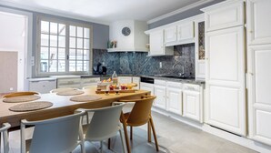 A modern kitchen with white cabinetry, a marble countertop, and a dining area with a wooden table and chairs.
