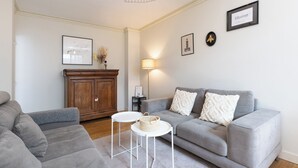 A living room with a grey sofa, a white side table, a lamp, and a cabinet.