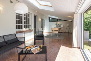 Een moderne woonkamer met een bank, een salontafel met fruit en drankjes, een fauteuil en een bureau met een lamp.