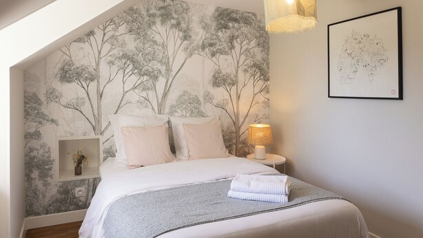 A bedroom with a bed, a nightstand, a lamp, and a wall with a tree mural.