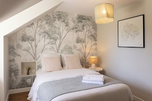 A bedroom with a bed, a nightstand, a lamp, and a wall with a tree mural.