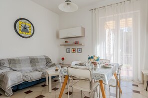 A living room with a sofa, dining table, chairs, a clock, and a window with curtains. - Cosy 95 sqm flat for 5 people, on the 1st floor of a building WITHOUT lift (there are stairs for access).The apartment is located in the Rebocco district of La Spezia, a quiet area well served by public transport. The city centre can be reached in about  (La Spezia)