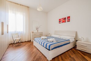Une chambre à coucher moderne avec un lit, des tables de chevet, une chaise et des œuvres d’art accrochées au mur.