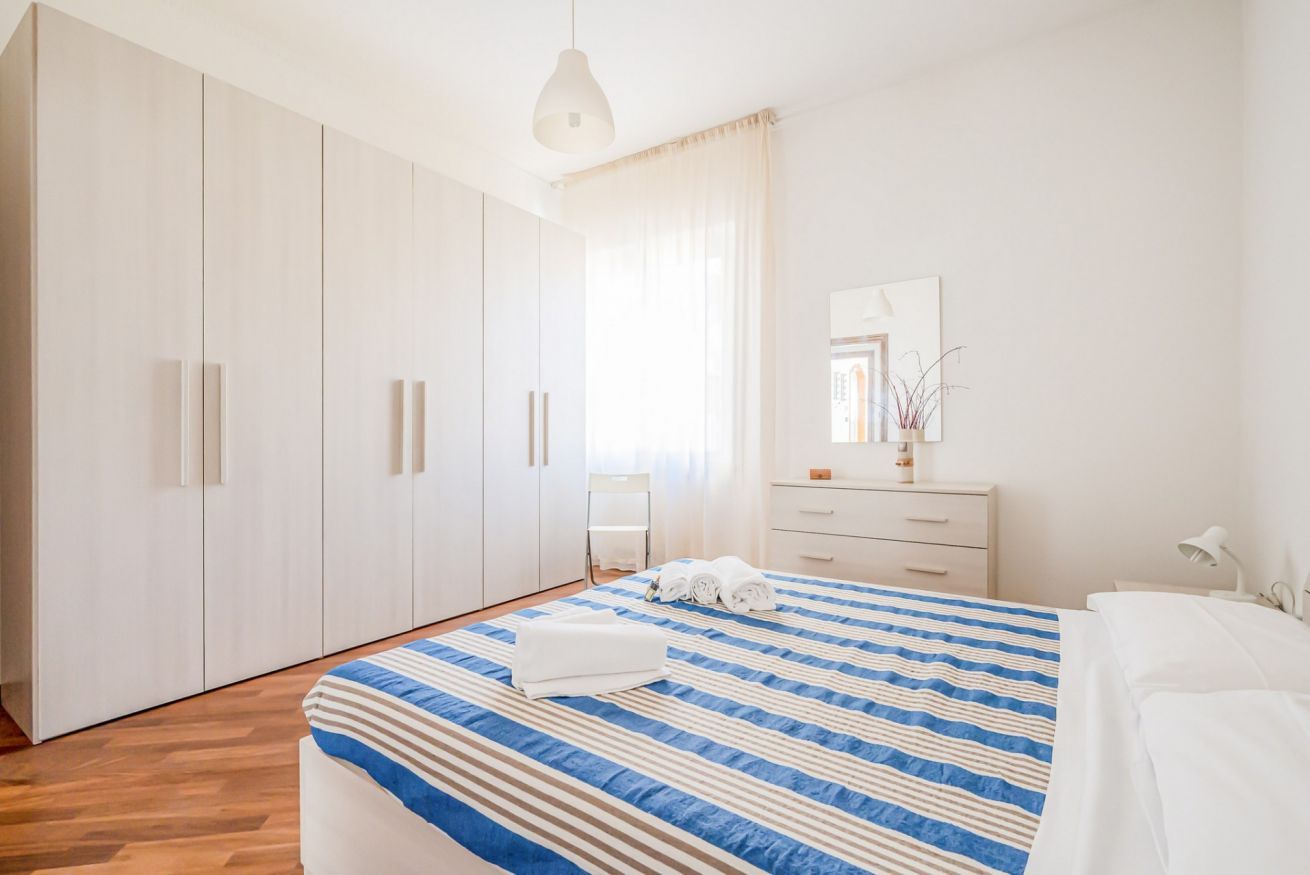 Une chambre à coucher comprenant un lit, une armoire, une commode, un miroir et une fenêtre avec des rideaux.