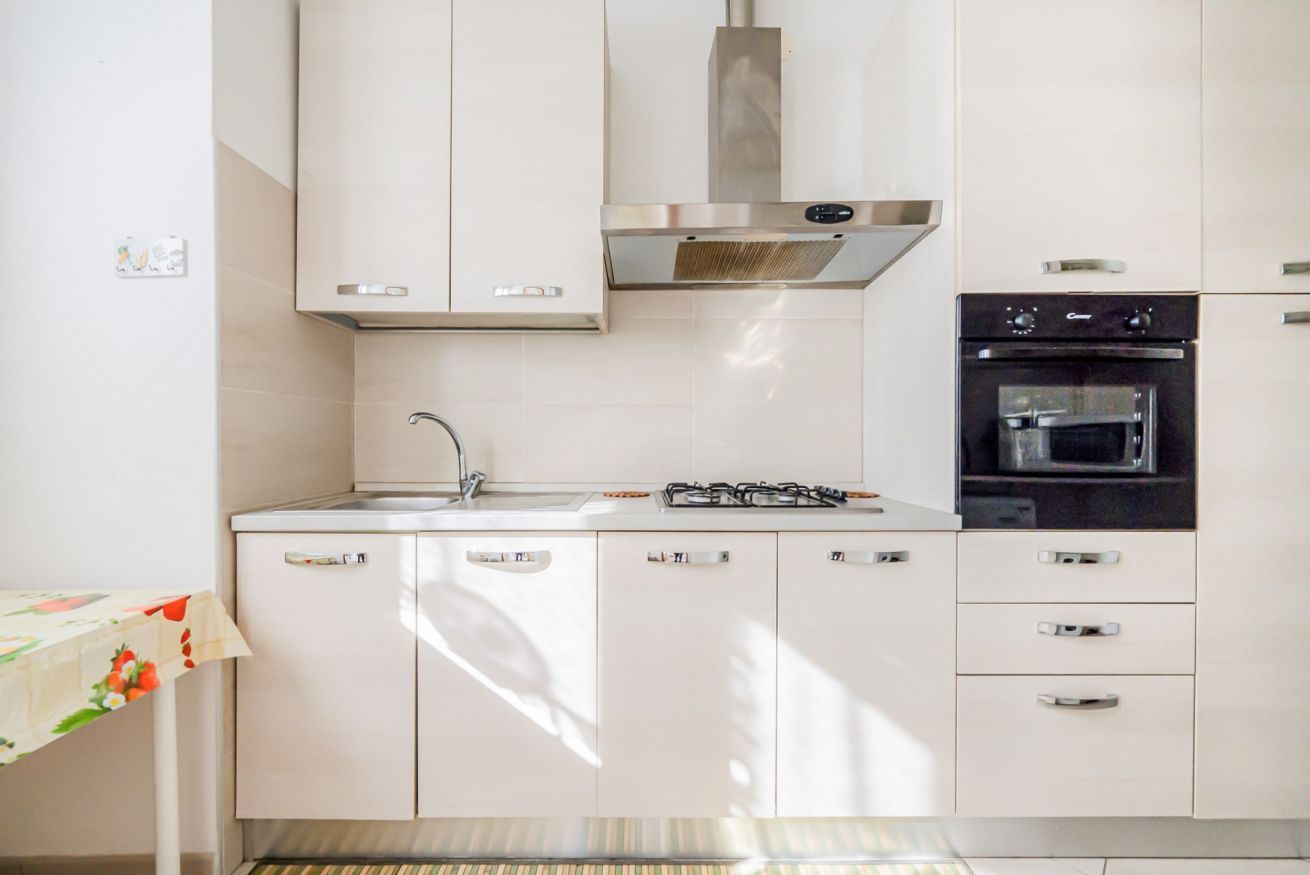 Una cucina moderna con mobili bianchi, una cappa in acciaio inossidabile, forno integrato e lavello.